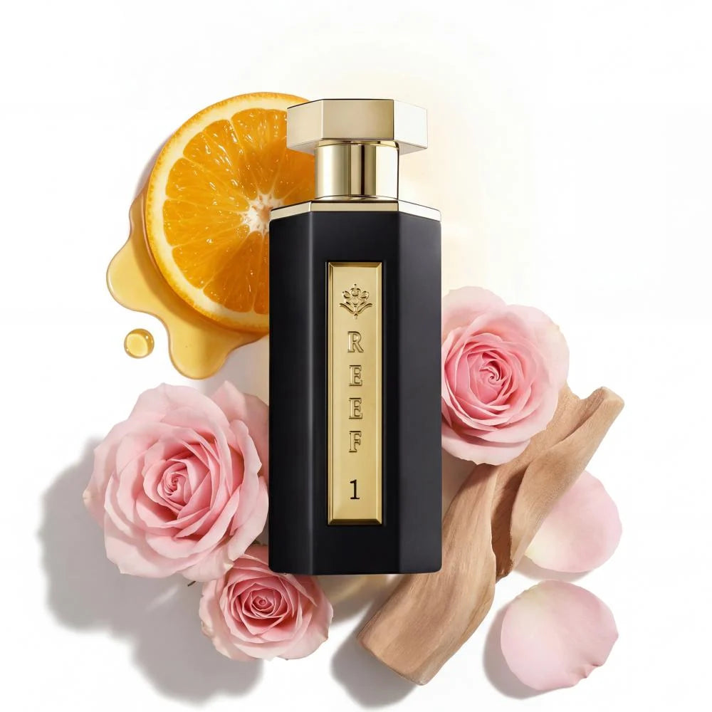 Luxury black perfume bottle with gold accents, surrounded by pink roses, orange slice, and oud wood